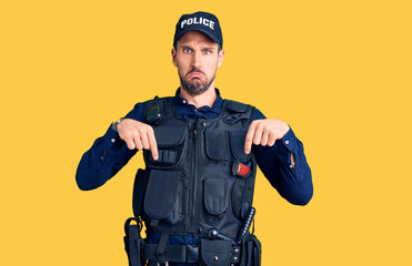 Young handsome man wearing police uniform pointing down looking sad and upset, indicating direction with fingers, unhappy and depressed.