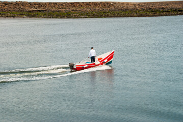Fototapeta premium A man standing in a moving small red motorboat on a calm day