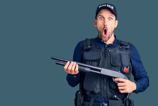 Young handsome man wearing police uniform holding shotgun scared and amazed with open mouth for surprise, disbelief face