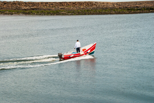 A man standing in a moving small red motorboat on a calm day