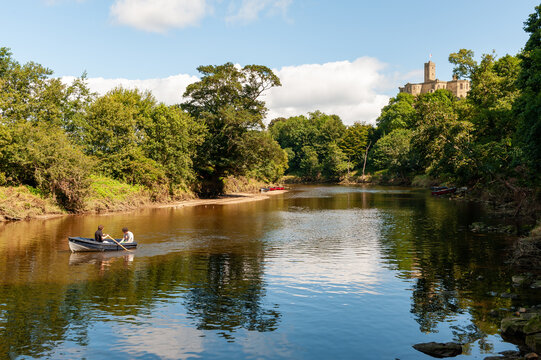 People in a rowing boat on the River Coquet with Warkworth Castle in the background on a sunny day
