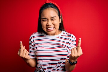 Young beautiful asian girl wearing casual striped t-shirt over isolated red background Showing...