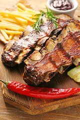 Tasty beef short ribs with vegetables and french fries on table, closeup