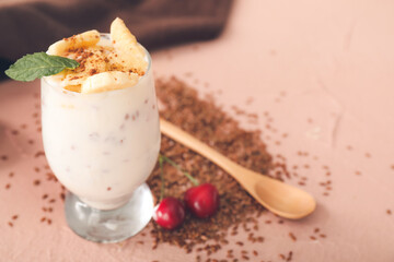 Glass of yogurt with fruits and flax seeds on color background