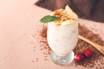 Glass of yogurt with fruits and flax seeds on color background