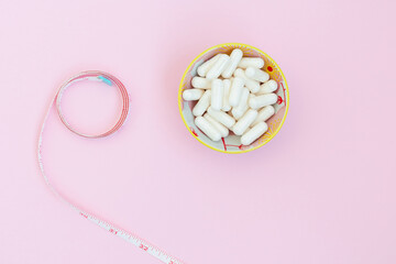 white capsules with white measuring tape on pink background.