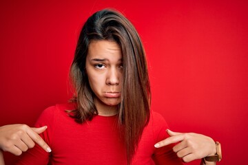 Young beautiful brunette girl wearing casual t-shirt over isolated red background Pointing down looking sad and upset, indicating direction with fingers, unhappy and depressed.