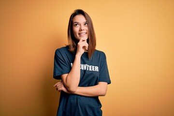 Young beautiful brunette girl doing volunteering wearing t-shirt with volunteer message word with hand on chin thinking about question, pensive expression. Smiling and thoughtful face. Doubt concept.