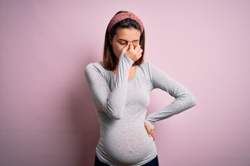 Young beautiful teenager girl pregnant expecting baby over isolated pink background tired rubbing nose and eyes feeling fatigue and headache. Stress and frustration concept.