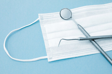 Medical mask and a set of metal dental instruments for dental care on a blue background. Selective focus