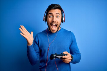 Young handsome gamer man with beard playing video game using joystick and headphones very happy and excited, winner expression celebrating victory screaming with big smile and raised hands © Krakenimages.com