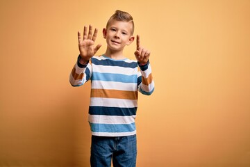 Young little caucasian kid with blue eyes wearing colorful striped shirt over yellow background showing and pointing up with fingers number six while smiling confident and happy.