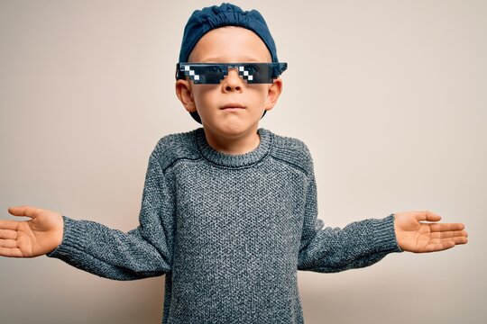 Young Little Caucasian Kid Wearing Internet Meme Thug Life Glasses Over Isolated Background Clueless And Confused Expression With Arms And Hands Raised. Doubt Concept.