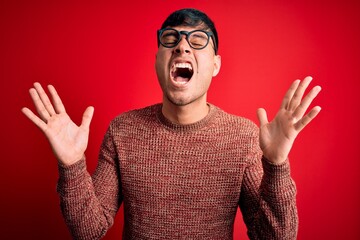 Young handsome hispanic man wearing nerd glasses over red background celebrating mad and crazy for...