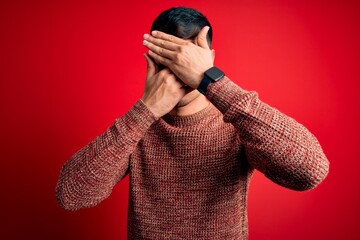 Young handsome hispanic man wearing nerd glasses over red background Covering eyes and mouth with...