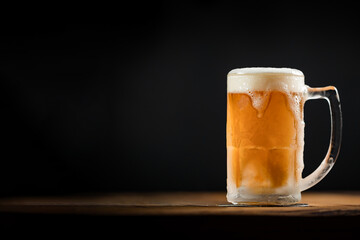 cold mug with beer, with overflowing foam, on wooden table and dark background