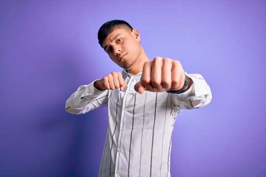 Young handsome hispanic man wearing elegant business shirt standing over purple background Punching fist to fight, aggressive and angry attack, threat and violence