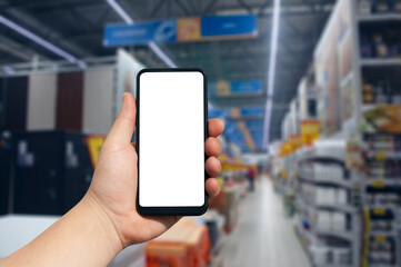 Online shopping using your phone. Mockup Smartphone with a white screen in hand close up on the background of shelving in a supermarket.