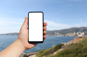 Time to travel. Smartphone in hand, against the background of the sea and the city under a sunny sky. Mock-up Technology.