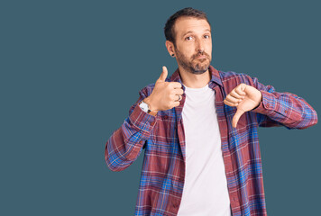 Young handsome man wearing casual clothes doing thumbs up and down, disagreement and agreement...