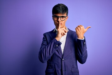 Young handsome business man wearing jacket and glasses over isolated purple background asking to be quiet with finger on lips pointing with hand to the side. Silence and secret concept.