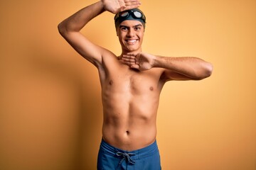 Young handsome man shirtless wearing swimsuit and swim cap over isolated yellow background Smiling cheerful playing peek a boo with hands showing face. Surprised and exited