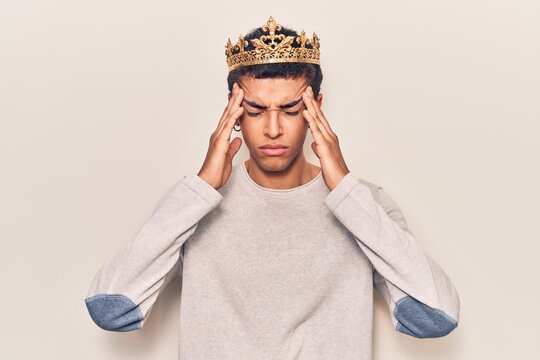 Young african amercian man wearing prince crown suffering from headache desperate and stressed because pain and migraine. hands on head.