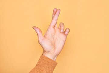 Hand of caucasian young man showing fingers over isolated yellow background gesturing fingers crossed, superstition and lucky gesture, lucky and hope expression