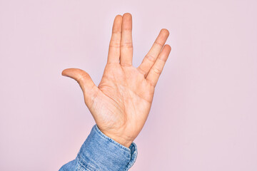 Hand of caucasian young man showing fingers over isolated pink background greeting doing Vulcan salute, showing hand palm and fingers, freak culture