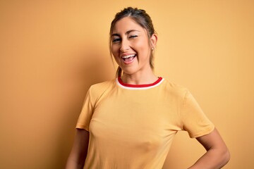Young beautiful athletic woman wearing casual t-shirt and ponytail over yellow background winking...