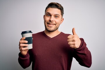 Young man with blue eyes drinking coffee from take away plastic bottle over isolated background happy with big smile doing ok sign, thumb up with fingers, excellent sign