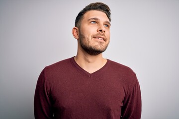 Fototapeta premium Young man with blue eyes wearing casual sweater standing over isolated background looking away to side with smile on face, natural expression. Laughing confident.