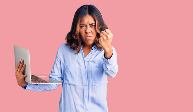 Young beautiful mixed race woman working using computer laptop annoyed and frustrated shouting with anger, yelling crazy with anger and hand raised