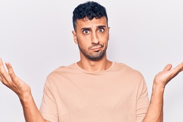 Young hispanic man wearing casual clothes clueless and confused with open arms, no idea and doubtful face.