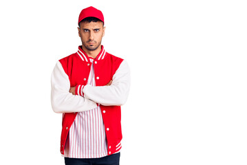 Young hispanic man wearing baseball uniform skeptic and nervous, disapproving expression on face with crossed arms. negative person.