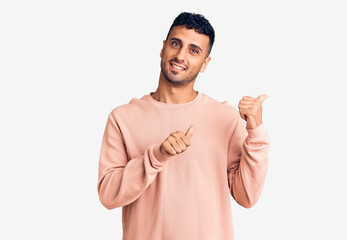 Young hispanic man wearing casual clothes pointing to the back behind with hand and thumbs up, smiling confident