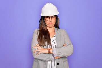 Professional woman engineer wearing industrial safety helmet over pruple background skeptic and nervous, disapproving expression on face with crossed arms. Negative person.