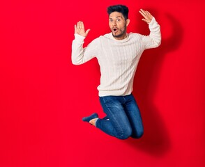 Young handsome latin man wearing casual clothes smiling happy. Jumping with smile on face over isolated red background