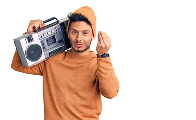 Handsome latin american young man holding boombox, listening to music doing italian gesture with hand and fingers confident expression