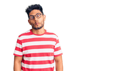 Handsome latin american young man wearing casual clothes and glasses making fish face with lips, crazy and comical gesture. funny expression.