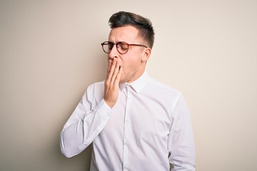 Young handsome business mas wearing glasses and elegant shirt over isolated background bored yawning tired covering mouth with hand. Restless and sleepiness.