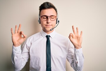 Young handsome caucasian business man wearing call center headset at customer service relax and smiling with eyes closed doing meditation gesture with fingers. Yoga concept.