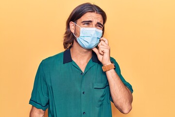 Young handsome man wearing medical mask serious face thinking about question with hand on chin, thoughtful about confusing idea