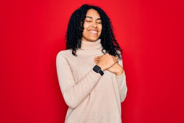 Young african american curly woman wearing casual turtleneck sweater over red background smiling with hands on chest with closed eyes and grateful gesture on face. Health concept.