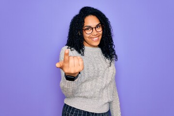 Young african american woman wearing casual sweater and glasses over purple background Beckoning come here gesture with hand inviting welcoming happy and smiling