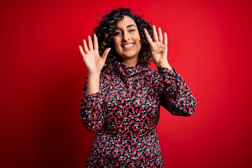 Young beautiful curly arab woman wearing casual floral dress standing over red background showing and pointing up with fingers number nine while smiling confident and happy.