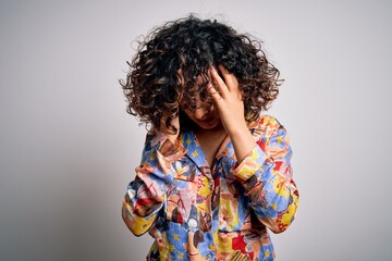 Young beautiful curly arab woman wearing floral colorful shirt standing over white background with hand on head for pain in head because stress. Suffering migraine.