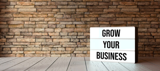Fototapeta na wymiar lightbox with message GROW YOUR BUSINESS on wooden floor in front of a brick wall