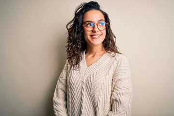 Beautiful woman with curly hair wearing casual sweater and glasses over white background looking away to side with smile on face, natural expression. Laughing confident.