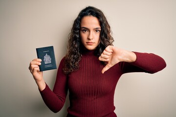 Young beautiful tourist woman with curly hair on vacation holding canadian canada passport with angry face, negative sign showing dislike with thumbs down, rejection concept